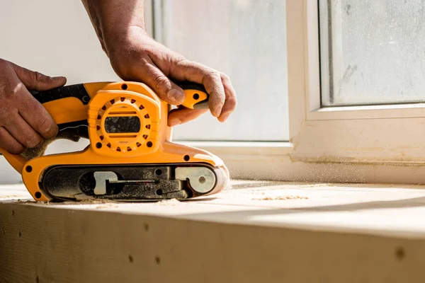 Carpenter's hands holding a belt sander against the window background — Stock Image Carpenter Hands Holding Belt Sander Window Background Stock Picture