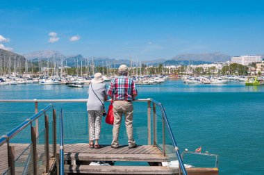 Pollensa, Balearic Adaları / İspanya; Mayıs / 19 / 2018: Güneşli bir günde Pollensa limanındaki rıhtıma bakan iki turist