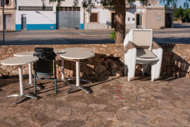 Açık masaların yanına istiflenmiş beyaz plastik sandalyeler. Coronavirus tarafından kapatılmış restoran işletmeleri