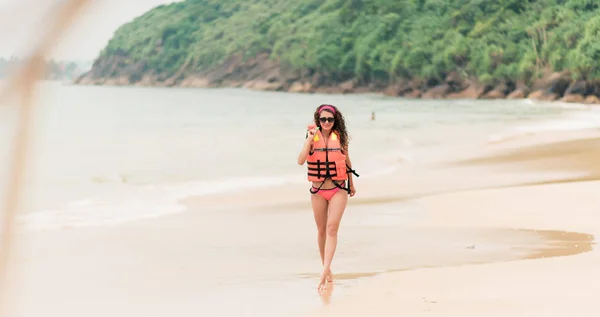 Glückliches Mädchen läuft in orangefarbener Schwimmweste am Strand in der Nähe der Brandung entlang — Stockfoto