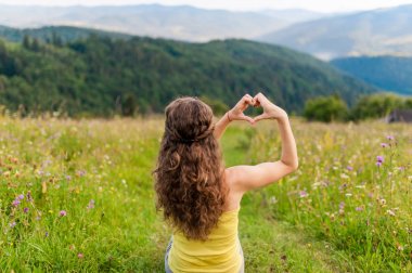 Genç kadın arka planda en iyi dağ manzarası olan bir kalp-şekil yapma.