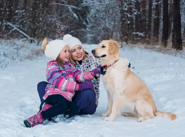 Cheerful mom and her cute daughter with their dog golden retriever in winter Royalty Free Stock Photos