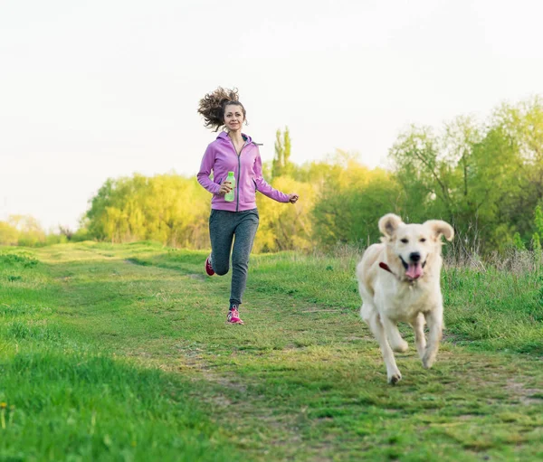 Joven chica bonita corriendo al aire libre en la primavera con el perro — Foto de Stock