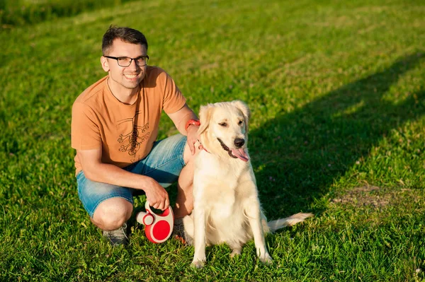 Młody mężczyzna tulenie golden retriever pies w lato na zewnątrz — Zdjęcie stockowe