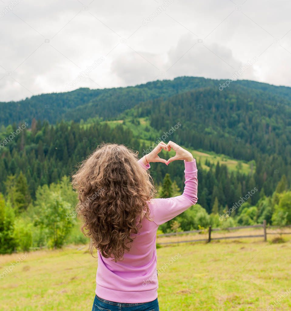 Freedom traveler woman standing with heart shaped hands and enjoy a wonderful nature. Yound girl show hand sign heart on top mountain with perfect view. travel concept