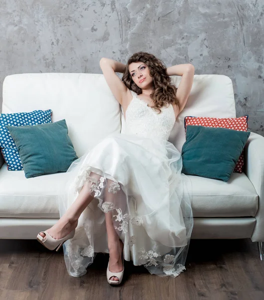 かわいい女性がスタジオで豪華なウェディング ドレスでソファーに長い髪との結婚式の後にリラックスします — ストック写真