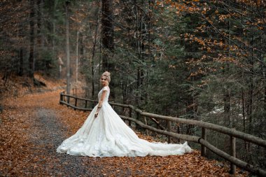 Dağların yakınında poz veren açık şifonlu gelinlikli güzel sarışın gelin.