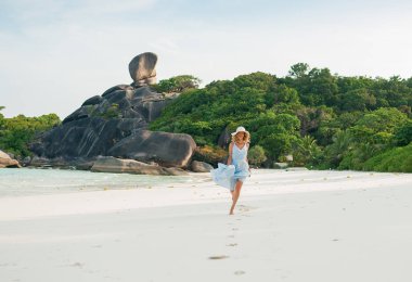 Mavi elbiseli genç bir kadın sahilde tek başına yürüyor. Tropik beyaz kum plajı. Similan Adaları, Andaman Denizi, Tayland
