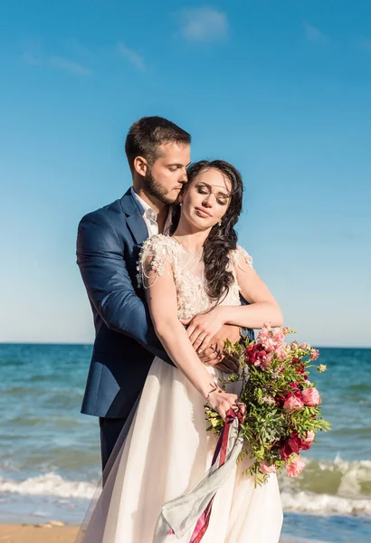 Mutlu yeni evliler mavi denizin arka planında el ele tutuşuyorlar. Kumsalda düğün yürüyüşü. Arka planda, mavi gökyüzü