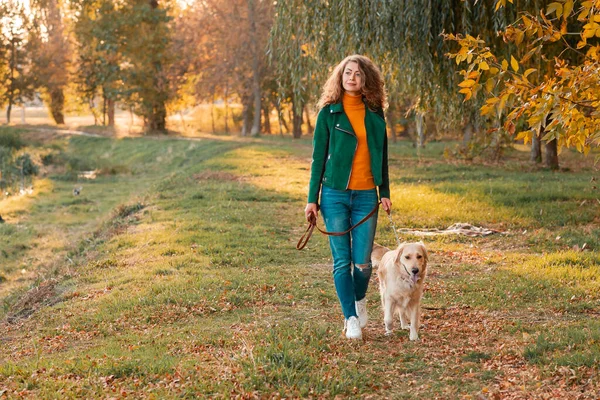 Sonbahar yapraklarında köpeğiyle genç kıvırcık kadın.