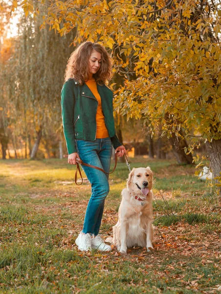 Młoda kręcona kobieta ze swoim psem Golden retriever jesienią liści — Zdjęcie stockowe