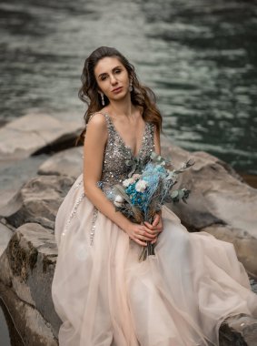 Lüks açık şifonlu gelinlik içinde, dağların yakınında poz veren boncuklarla işlenmiş güzel esmer gelin. Karpat Dağları 'nda düğün. Lüks elbiseli romantik gelin dışarıda poz veriyor.