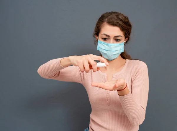 戴医疗面罩的女性使用清洁剂凝胶在灰蒙蒙的背景下消毒双手 人们洗手以保护自己的生命不受病毒和感染 — 图库照片