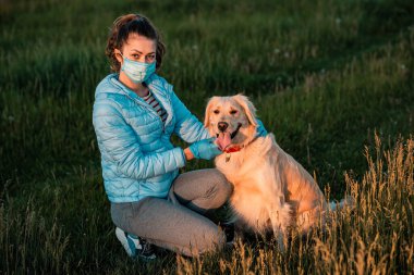 Büyük Golden Retriever köpeğini doğa parkında tıbbi bir maskeyle koronavirüsten korumaya çalışan bir kız. Salgın hastalık ve salgınlara karşı korunma. Covid 19