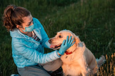 Genç yetişkin kız ve onun Golden Retriever köpeği güvenlik maskesi takıyor, birlikte oturuyorlar. Coronavirüs salgını, qaurantine, çevre kavramı.