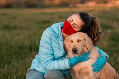 Bahar parkında köpeğini kucaklayan kıvırcık bir genç kadının portresi. Genç bir kadın köpeğiyle oturuyor. Sağlık hizmetleri koruma kavramı.