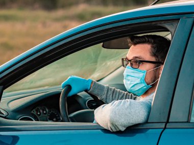Koruyucu maskeli ve eldivenli bir adam araba kullanıyor. Adam arabayla gelir, kendini virüsten korur, elinde direksiyon tutarak. Koronavirüs enfeksiyonunun önlenmesi, covid-19.