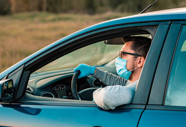 Bearded man wearing medical gloves, protects himself from bacteria and virus, holds car steering wheel. Poses in own transport car. Covid-19 concept