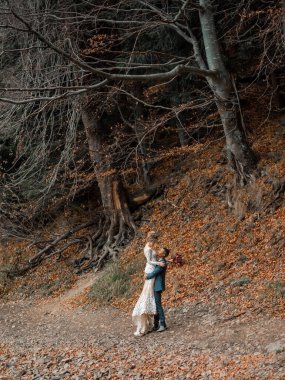 Afrikalı damat ve beyaz gelin taze çiçeklerle boho tarzında kucaklaşıyorlar. Gelin ve damat elleriyle gülüyor ve gülümsüyor.