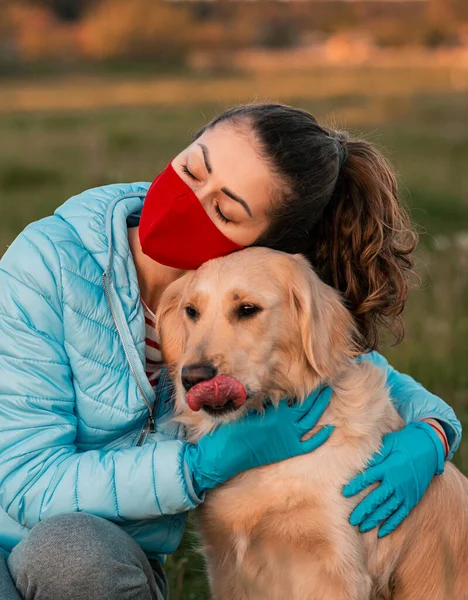 Tıbbi korumalı yüz maskesi takan Golden Retriever köpeği kucaklayan kadın. Tıbbi maskeli bir köpek kameraya bakıyor. Evcil hayvan hijyen kavramı
