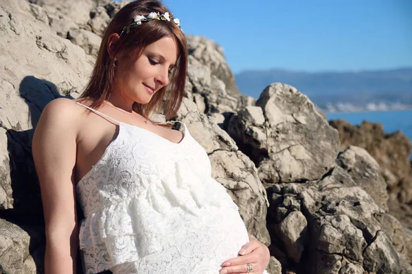 Beautiful pregnant woman outdoor in white dress with a floral crown style near the sea — Stock Photo, Image