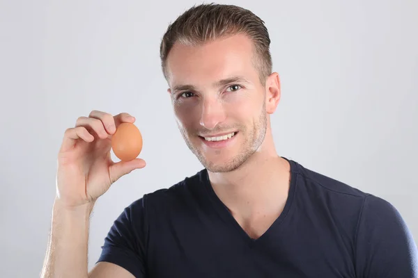Handsome blond man on smiling face holding egg in studio — Stock Photo, Image