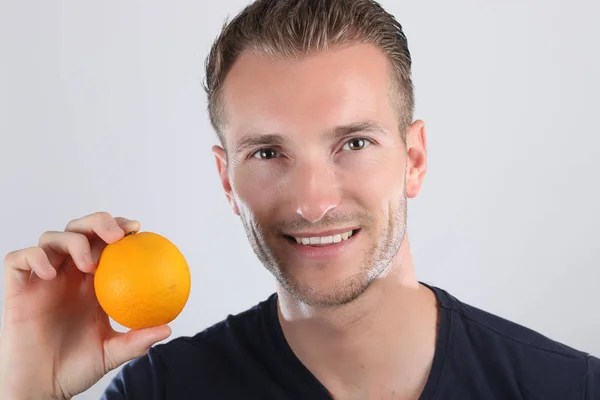 Living food koncept. Porträtt av glad ung man som bär blå t-shirt innehav orange i hand — Stockfoto