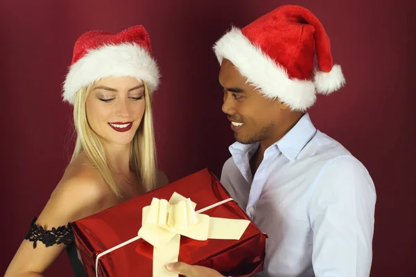 赤い背景の上のクリスマスのギフトを提供する若いカップル — ストック写真