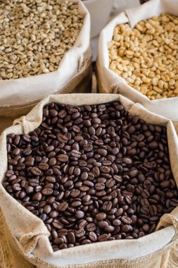 Yeşil ve kahverengi kahve çekirdekleri kavrulmamış ve siyah kahve çekirdekleri çuvalda.