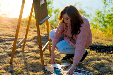 genç sanatçı bir deniz manzarası günbatımında çizer.