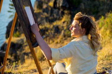 genç sanatçı bir deniz manzarası günbatımında çizer.