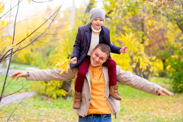 Hombre con hijo joven en los hombros Autumn Park — Foto de Stock