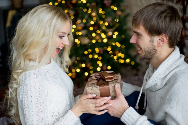 Glückliches Liebespaar in weißen Pullovern beschenkt sich gegenseitig — Stockfoto
