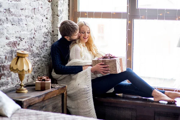 Šťastný pár milenců v pulovry obdarovat navzájem sedí — Stock fotografie