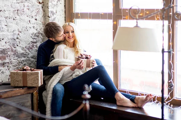 Casal feliz de amantes em pulôveres dar uns aos outros presentes sentados — Fotografia de Stock