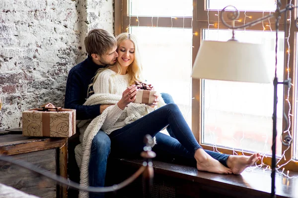 Feliz pareja de amantes en pullovers dar unos a otros regalos sentado —  Fotos de Stock