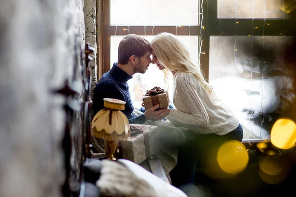 Щаслива пара закоханих в пуловерах дарує один одному подарунки сидячи — стокове фото