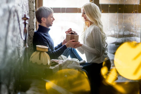 Happy couple of lovers in pullovers give each other gifts sitting — Stock Photo, Image