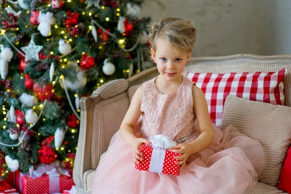 Liten flicka med julklapp sitter nära träd — Stockfoto