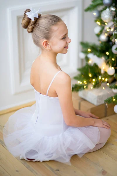 Young ballet dancer sitting near Christmas tree