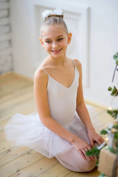 Young ballet dancer sitting near Christmas tree