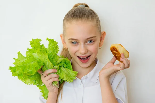 Young girl chooses between a lettuce and baking isolated — Stock Photo, Image