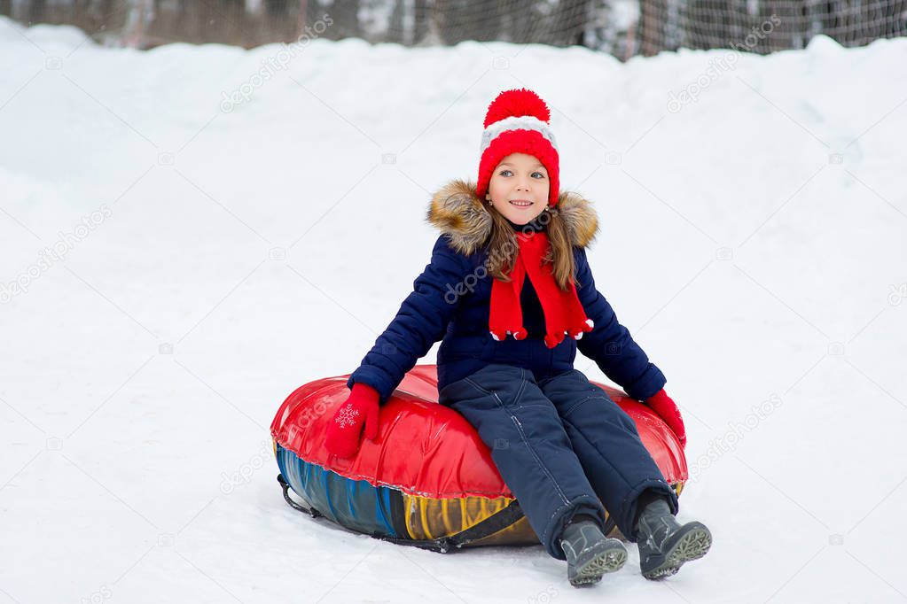 Little girl on snow tubes downhill at winter day