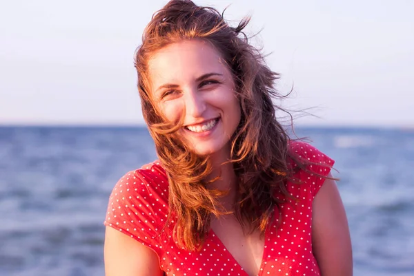 Jong meisje in een rode jurk glimlachend op de achtergrond van de zee — Stockfoto