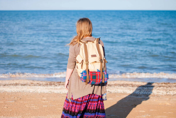 Девушка стоит в стороне и смотрит на море. Девушка-хиппи смотрит на море. Женщина с бутылкой вина у моря. Хиппи девушка со старым рюкзаком и бутылкой вина
.