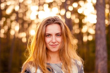 Gün batımında ormanda gülümseyen genç yalnız kız.