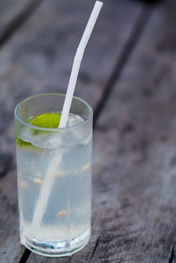 Bir bardak limonata ve ahşap bir masa üzerinde bir saman. Alkol kireç ve tonik sert ahşap zemin ile kokteyl.