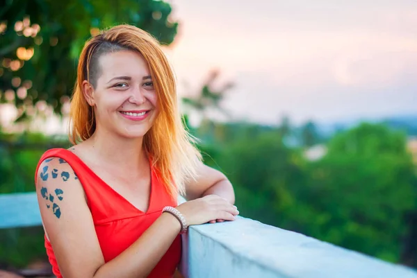 Kırmızı bir elbise ve dövmeli gülüyor bir yaz Restoran verandada güzel kızıl saçlı kız