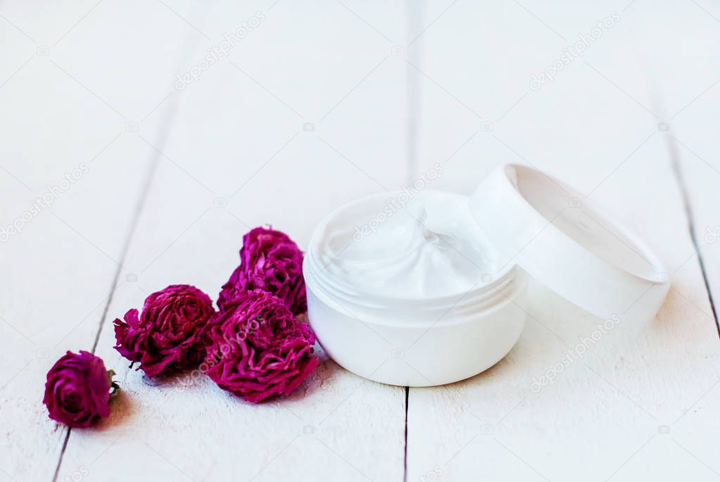 Absolutely white jar with cream for dry skin on a white wooden background with dry rose flowers