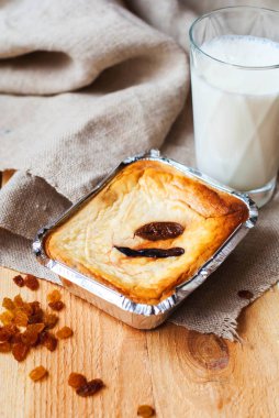 Güveç cottage cheese den ahşap bir masa üzerinde bir bardak süt ile bir fırında pişmiş. Peynirli incir üzerinden bir bardak süt ile kahvaltı için folyo pişirme için bir form ile.